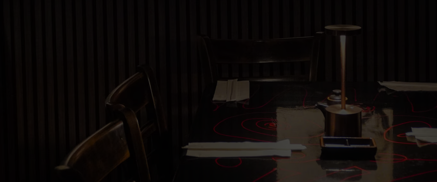 A moody table setting inside Tokyo Club Sushi Speakeasy with Japanese scroll art and dark slatted walls.